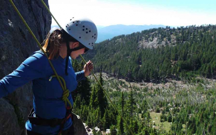 a rock climbing student looks town on tree covered hills during an outward bound course